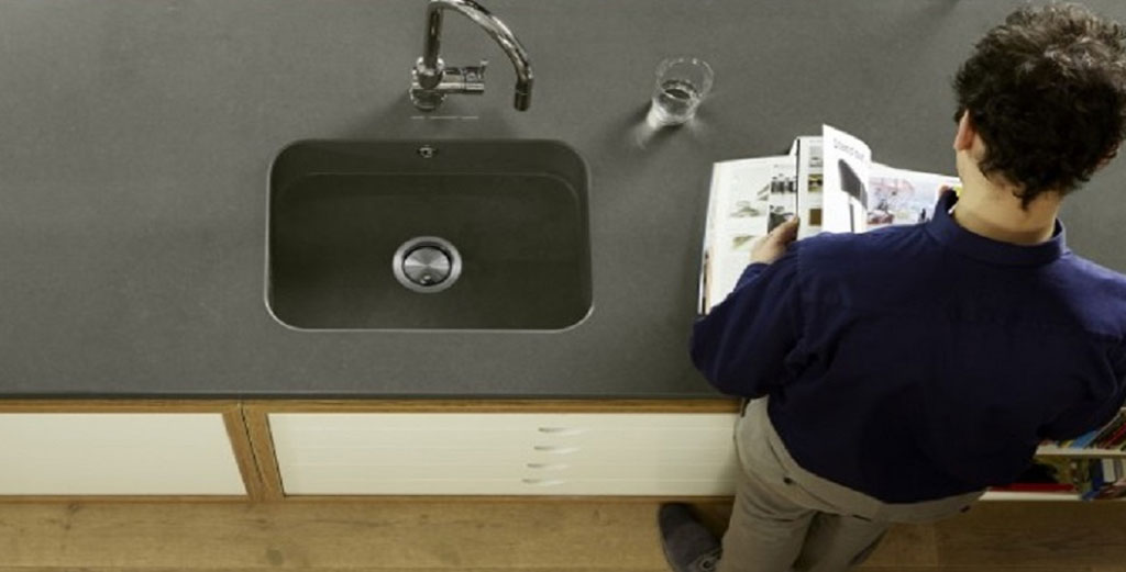 Overhead view of a modern kitchen worktop with a built-in sink and a person reading a magazine
